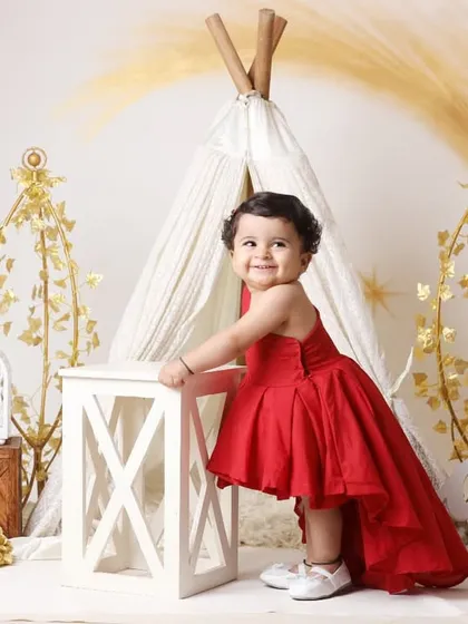 Celebrating a first birthday is a momentous occasion. We create stunning setups like this one, featuring a beautiful red gown and elegant props, to make your little one's milestone portrait truly special.