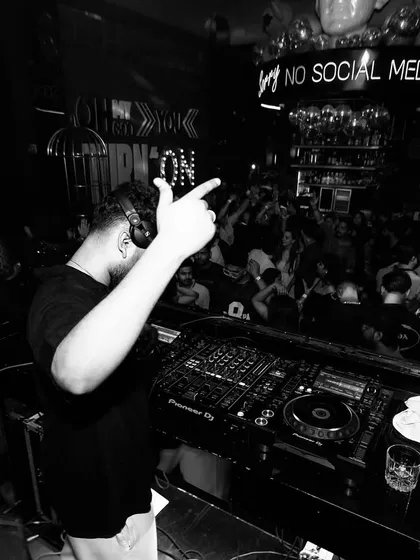 A black and white shot from behind the decks, with the crowd fully engaged. The "NO SOCIAL MEDIA" sign in the background adds to the exclusive, in-the-moment feel of the party.