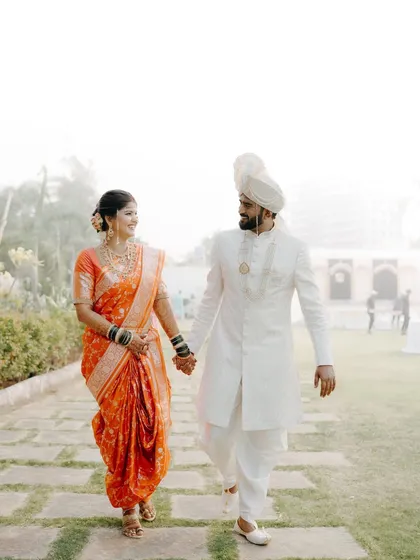A walk to remember. This full-length shot captures a Maharashtrian couple in their wedding attire, holding hands as they walk through a garden path, creating a serene and timeless wedding portrait.