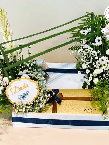 A personalized trousseau hamper for "Dadu," showcasing a modern, structured floral arrangement with fresh white chrysanthemums and tuberoses. It's a perfect blend of tradition and contemporary design.