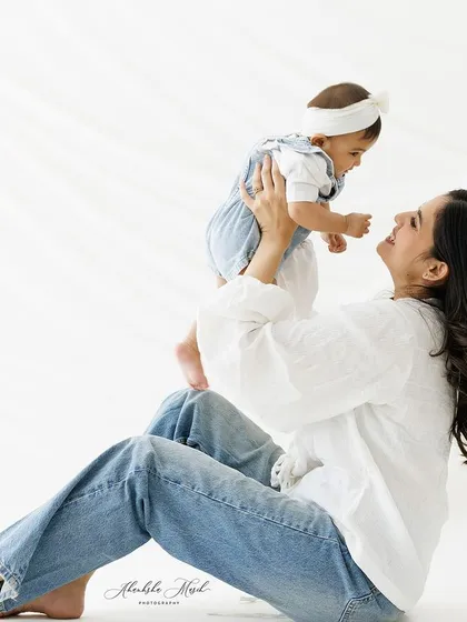 A playful and loving moment. The mother lifts her baby, sharing a look of pure adoration. The bright, airy setup makes the image feel light and joyful.