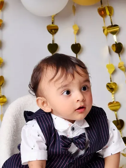 A sweet close-up of the birthday boy, capturing his curious expression against the backdrop of shimmering gold heart decorations.