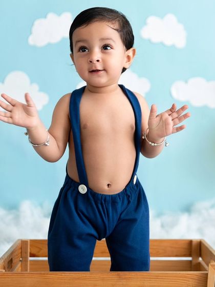 A baby boy stands in a wooden crate against a sky-themed backdrop, showing off his ability to stand.