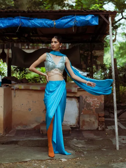 The full look, showcasing the convenience and high-fashion impact of a pre-draped sari. The contrast of the blue sari against the rustic backdrop makes the color pop even more.