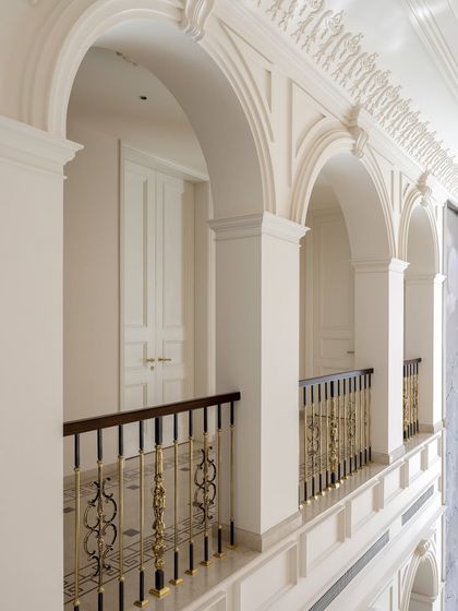 The upper gallery of The Ivory Royale features a procession of classical arches and detailed cornices. The intricate metalwork of the balustrade adds a layer of decorative artistry, reinforcing the home's palatial and luxurious character.