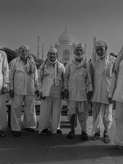 A group of elderly men in traditional white attire stand for a portrait in front of the Taj Mahal, a dignified and timeless black and white photograph.