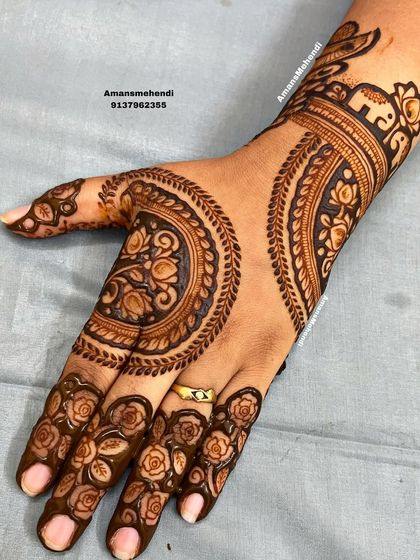 A close-up of the circular floral back-of-hand design. The fingers are decorated with rose patterns, and a small elephant on the wrist adds a traditional touch.