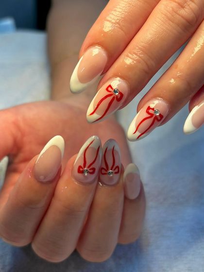 A closer look at the sweet red ribbon nail art on a classic French manicure base. The tiny rhinestone adds the perfect finishing touch.