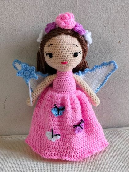 A beautiful fairy doll in a pink dress with little butterflies. She has wings and a magic wand with a star.
