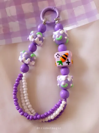 This purple and white beaded charm features cute, cake-like beads and a fun cartoon character bead, perfect for a whimsical, sweet style.
