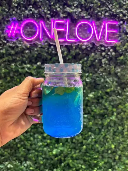 Our signature Blue Curacao Mojito, a refreshing non-alcoholic drink. It's the perfect vibrant cooler to enjoy against the backdrop of our cafe's green wall and neon sign.