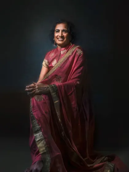 This full-length portrait showcases the elegant drape of a pink sari. The lighting creates a dramatic, artistic effect that emphasizes both the subject's poised demeanor and the beauty of the traditional garment.