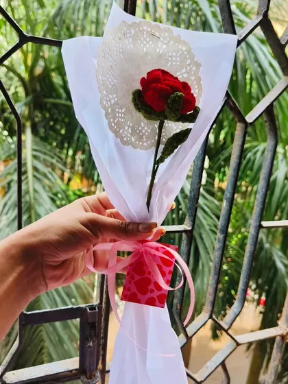 A single red crochet rose, beautifully wrapped in white paper with a doily and a heart-patterned ribbon. It proves that even a single flower can be a grand gesture.