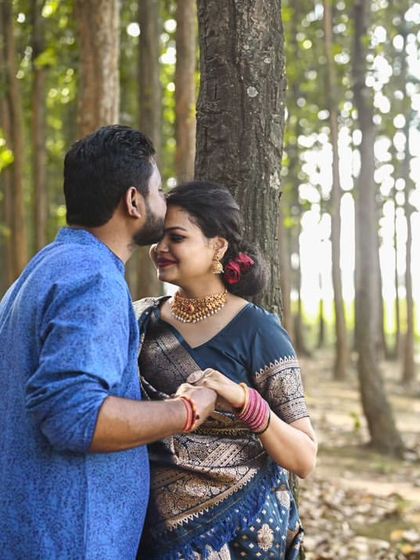 A tender moment with a kiss on the forehead. The sunlight filtering through the trees adds a warm, romantic glow to this forest maternity portrait.