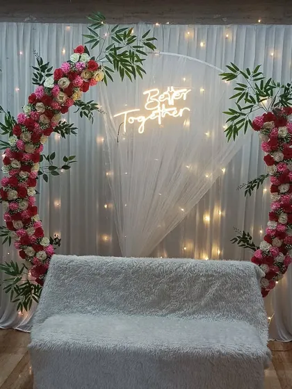 A semi-circular floral arch with a neon sign, perfect for a modern engagement party. We added bamboo-like greenery to give this popular design a unique touch.