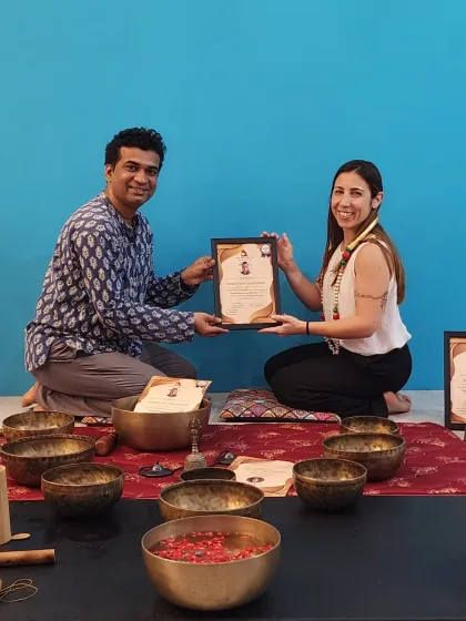 A student receives her certification, marking the end of an intensive training in sound therapy. Her smile reflects the fulfillment of the journey.