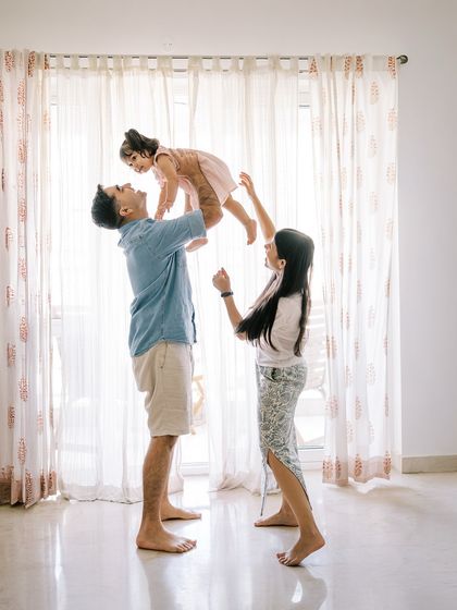 Home shoots are for being yourselves. A father lifting his daughter high in front of a bright window creates a beautiful silhouette and a moment of pure joy.