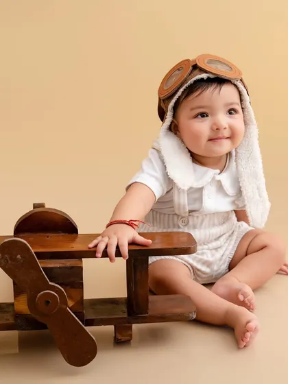 Ready for takeoff. This adorable baby pilot sits next to his wooden airplane, looking sweet and adventurous.