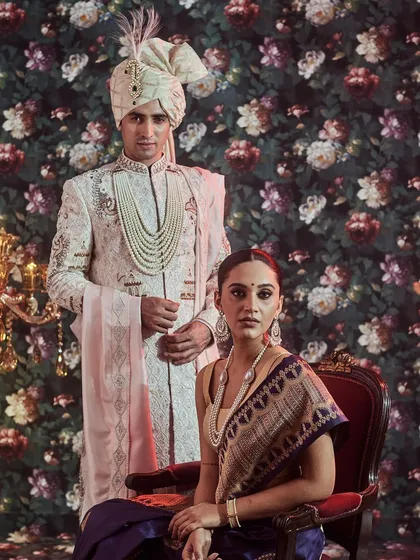 A vision of regal sophistication. Here, we present a coordinated couple's look, featuring a bride in a traditional navy blue Banarasi saree and a groom in an intricately embroidered off-white sherwani with a matching safa.