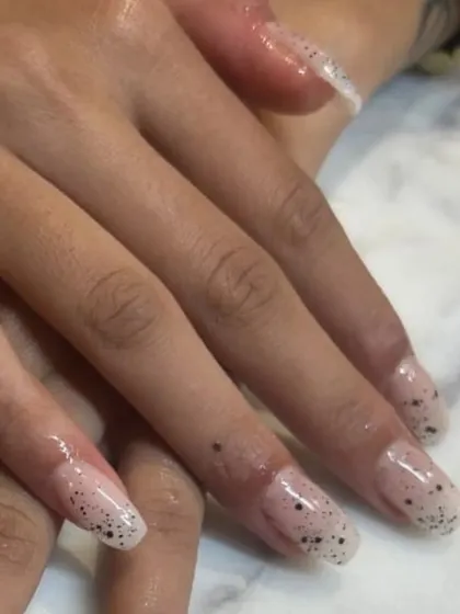 A closer view of the delicate speckled nail art on these long, clear extensions. It's a minimalist design with a touch of personality.