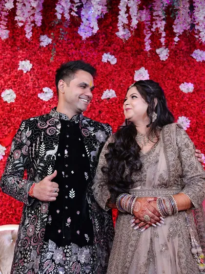 A happy portrait of a couple at their engagement, smiling at each other against a red floral backdrop.