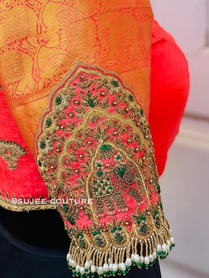 A close-up of a stunning sleeve design. This features a traditional 'Jharokha' window motif with an elephant, intricately embroidered with zardozi and beads, and finished with pearl tassels.