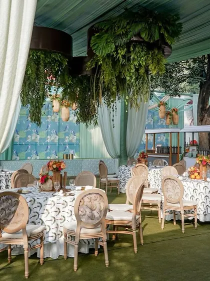 A garden brunch setup with mint green drapes, cane-back chairs, and hanging rattan lights, creating a breezy and beautiful atmosphere.