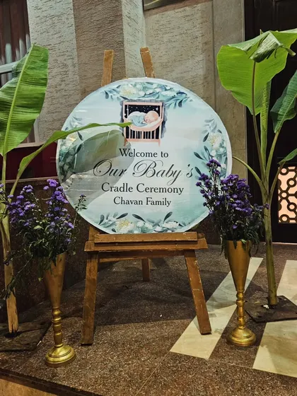 A personalized welcome sign is a lovely touch for any ceremony. Here, a custom circular sign for a cradle ceremony is flanked by traditional banana plants and floral arrangements, greeting your guests with warmth.