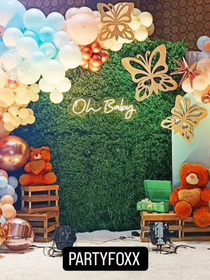 A butterfly-themed baby shower with a green hedge wall, a neon "Oh Baby" sign, and a beautiful arch of pastel and rose gold balloons.