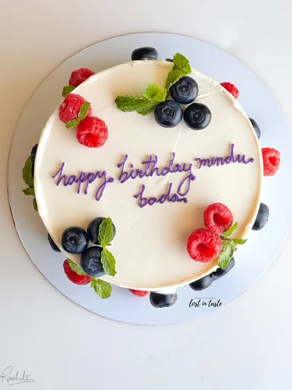 A simple yet beautiful celebration cake with chocolate buttercream, decorated with fresh raspberries, blueberries, and mint leaves for a pop of color and flavor.