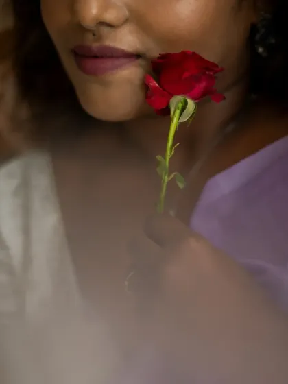 A creative close-up focusing on the model's lips and a single red rose. The soft focus and intimate framing create a romantic and slightly mysterious portrait.