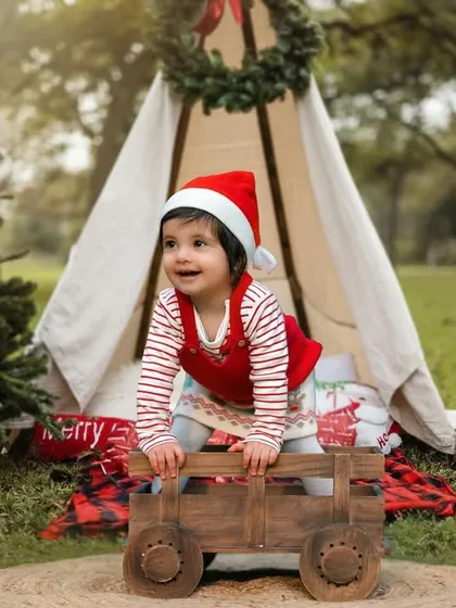 A very merry Christmas shoot. This little one is full of holiday cheer in her Santa hat, enjoying a festive outdoor setup with a teepee and presents.