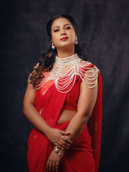 A powerful and elegant portrait in a red saree. The addition of a pearl shoulder piece adds a unique, high-fashion element to the traditional attire.