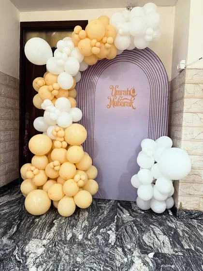 I also provide decorations for religious occasions. This 'Umrah Mubarak' setup features an elegant purple arch backdrop with custom lettering, framed by a beautiful arrangement of pastel yellow and white balloons.
