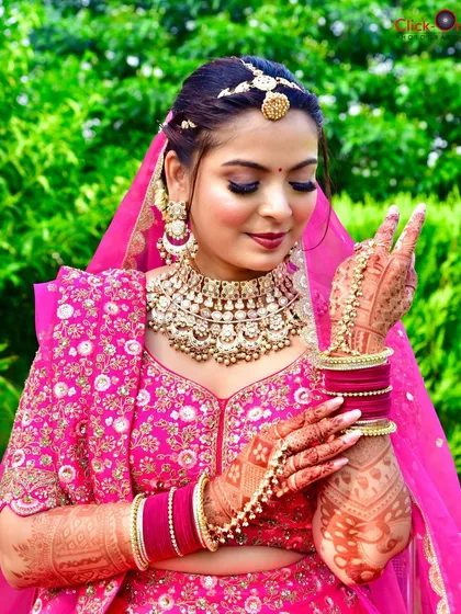 A beautiful outdoor bridal portrait. The bride, dressed in a vibrant pink lehenga, shows off her intricate mehndi with a playful gesture.