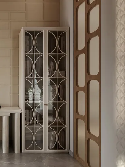 This image highlights the elegant storage solutions in a neutral-toned bedroom. A glass-front cabinet with an intricate geometric overlay provides a beautiful display for books, balancing the room's modern and classic elements.