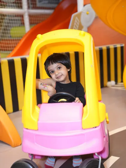 A little boy takes the wheel of his pink and yellow car, exploring the play area at his own pace.