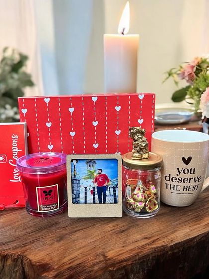 A cozy and romantic gift set for him, featuring a "You Deserve the Best" mug, a scented candle, love coupons, a personal photo frame, and a jar of chocolates.