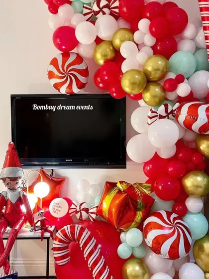 I also do cozy Christmas decor for homes. This festive balloon arrangement surrounds a TV, incorporating an elf figure, candy cane props, and gift boxes to create a fun holiday corner.