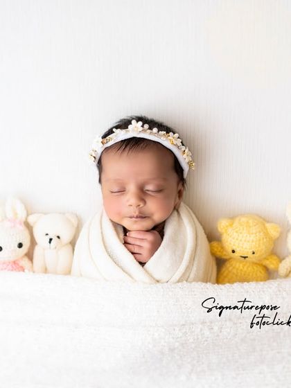 A sweet newborn wrapped in white and lined up with a row of adorable stuffed animals.