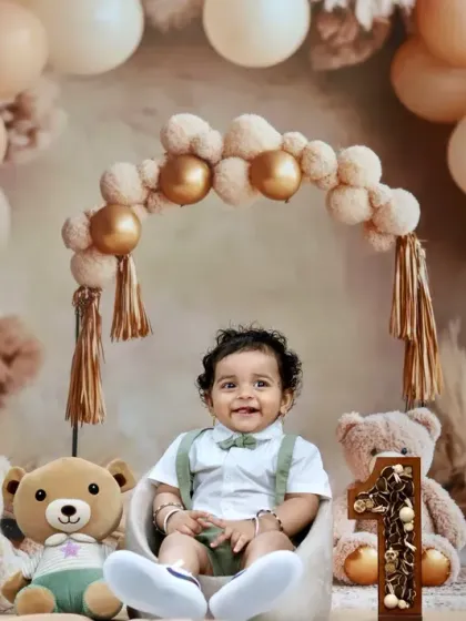 This baby boy flashes a charming smile, sitting in a circle of teddy bears during his cozy and cute birthday session.