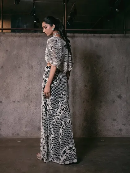 A modern monochrome look with a pearl-embellished crop top, straight skirt, and a dramatic cape.