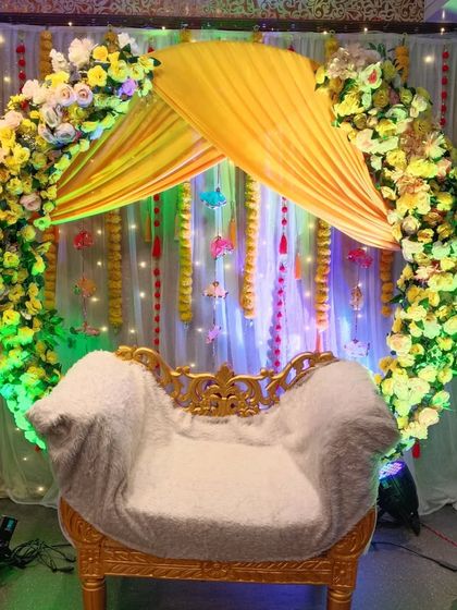 A circular arch backdrop for a Haldi ceremony, decorated with yellow and white flowers. The yellow canopy over the seat and the fairy lights create a bright and cheerful focal point.