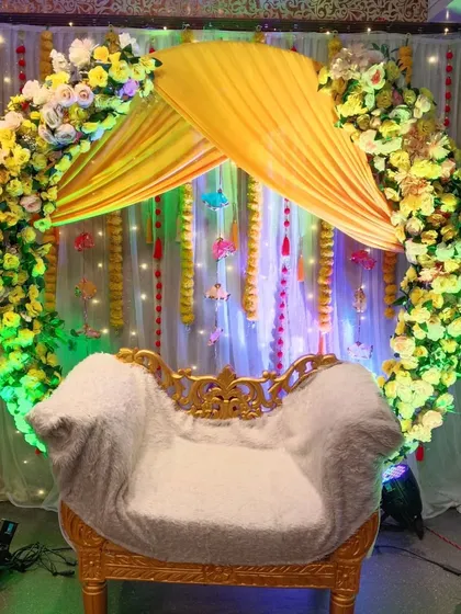 A circular arch backdrop for a Haldi ceremony, decorated with yellow and white flowers. The yellow canopy over the seat and the fairy lights create a bright and cheerful focal point.
