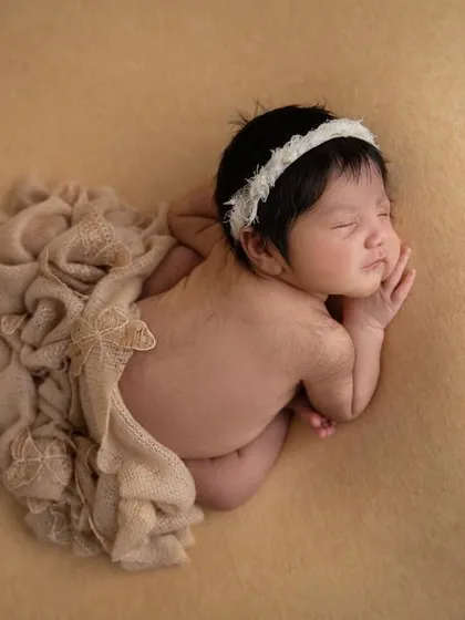 A top down view of the 'taco' pose, showing the baby's back and the soft folds of the neutral colored wrap.