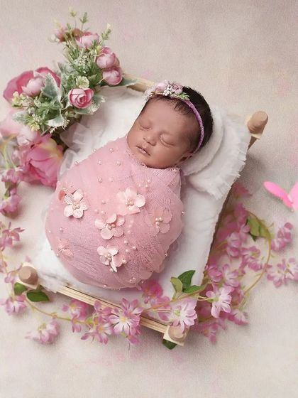 Sleeping peacefully on a tiny bed adorned with pink blossoms. This setup is all about delicate details, from the floral wrap to the butterfly accent, creating a dreamy and feminine newborn portrait.