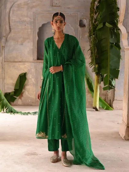 This emerald green angrakha set flows like poetry in motion. The wrap silhouette, delicate embroidery, and striped dupatta create a look that is both comfortable and effortlessly festive.