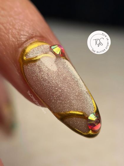 A close-up showing the detail of the sculpted gold lines and iridescent crystal accents on a shimmery, textured base.