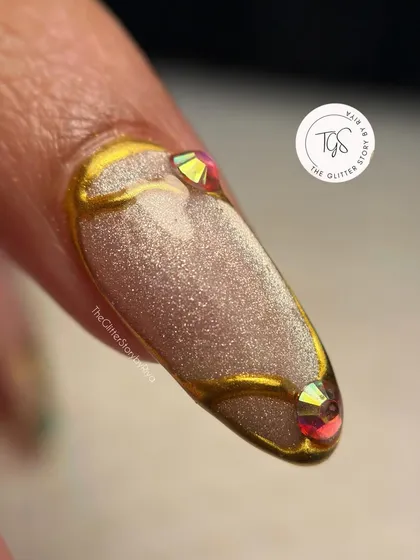 A close-up showing the detail of the sculpted gold lines and iridescent crystal accents on a shimmery, textured base.