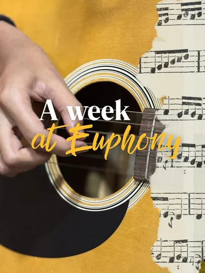 A close-up of a student's hands on an acoustic guitar, with sheet music in the background. This image captures the essence of a week at Euphony: practice and passion.